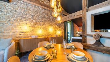 A dining area with a stone wall, wooden beams, and hanging light fixtures.