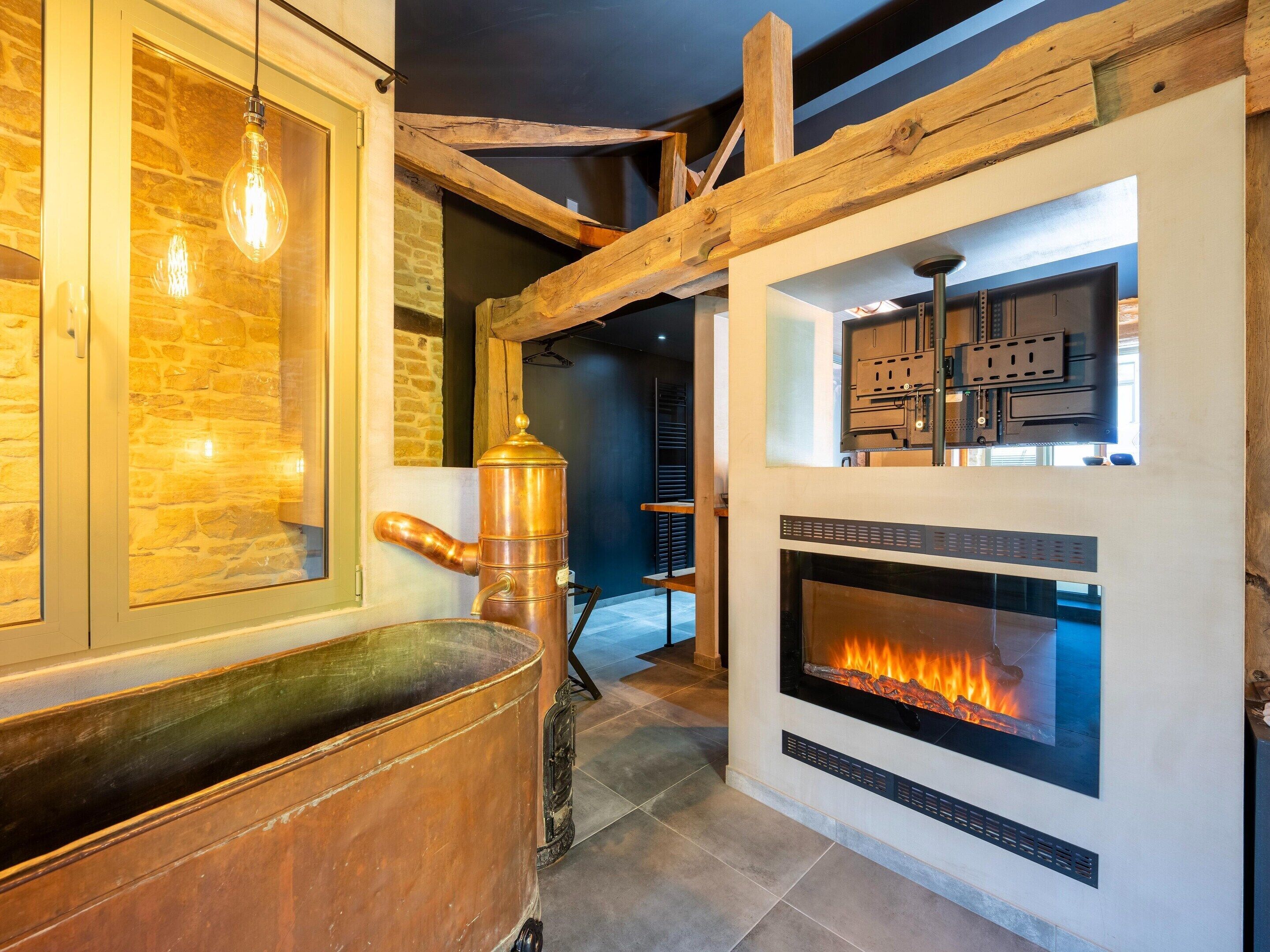 A modern interior with a stone wall, a copper boiler, and a fireplace with a visible fire.