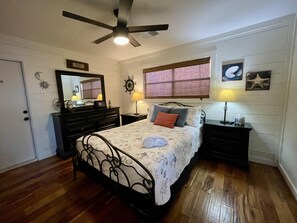 A bedroom with a bed, a dresser, a vanity, a ceiling fan, a window with blinds, and wall decorations. - Kitty by the Sea! Waterfront + Great Fishing! Charming 2br/2ba pet friendly home (Rockport)