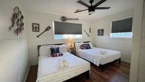 Ein Zimmer mit zwei Betten, einem Deckenventilator, einem Fenster mit Jalousien und maritimer Dekoration.
