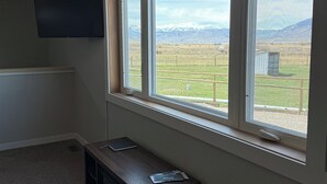 A room with a large window offering a view of a mountainous landscape. A flat-screen TV is mounted on the wall.