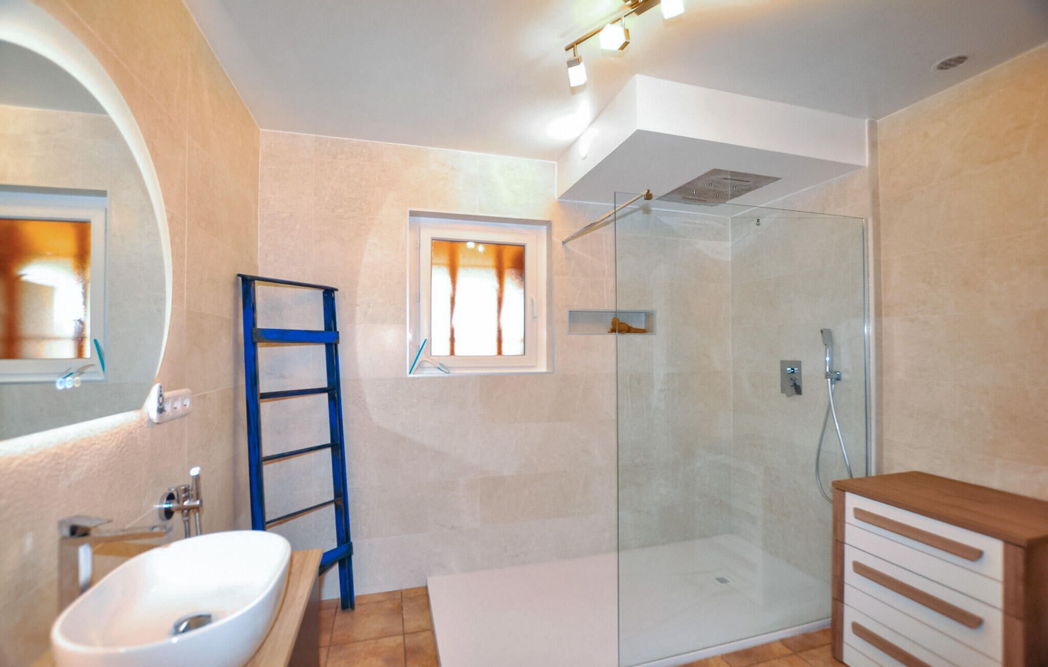 A modern bathroom with a glass-enclosed shower, a white sink, and a wooden cabinet.