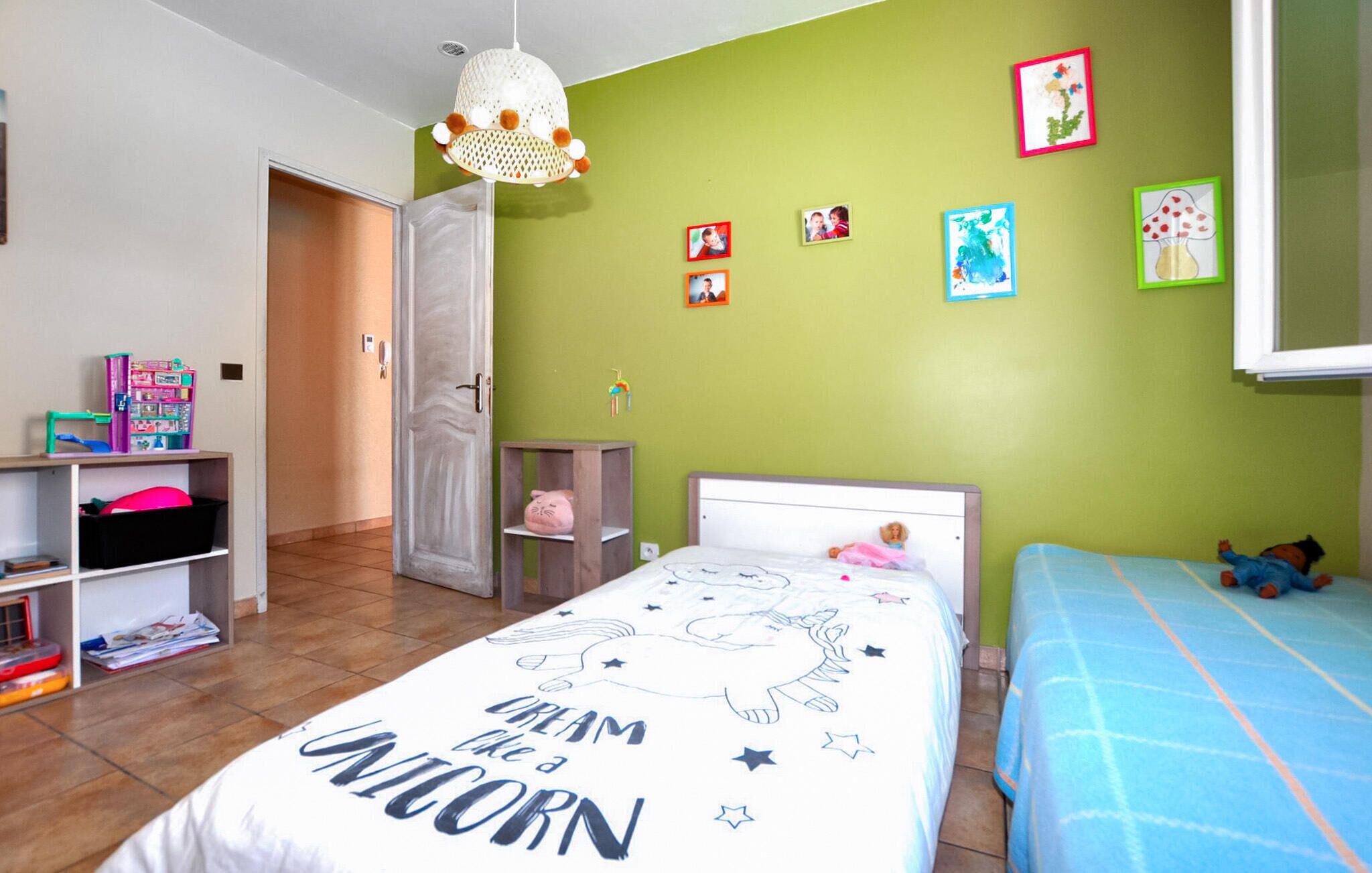 Une chambre à coucher avec un lit, une table de chevet, une étagère remplie de jouets et un mur vert orné de tableaux.
