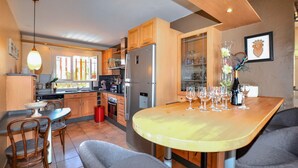 A modern kitchen with wooden cabinets, a stainless steel refrigerator, and a dining area with a table set for a meal. - Awesome home in Saleilles (Saleilles)