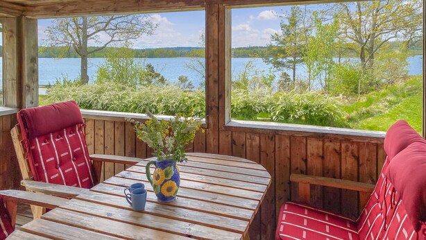 A wooden deck with a table and chairs, overlooking a lake with trees and a clear sky. - 1 bedroom beautiful home in Tranås (Tranås)