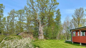 A red cabin with a grassy yard, surrounded by trees and a large rock formation. - 1 bedroom beautiful home in Tranås (Tranås)