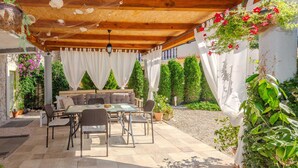 An outdoor patio with a wooden pergola, a dining table with chairs, and a seating area with cushions.