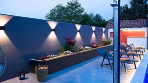 An outdoor patio area with a dark wall, solar lights, a planter with flowers, and outdoor seating.