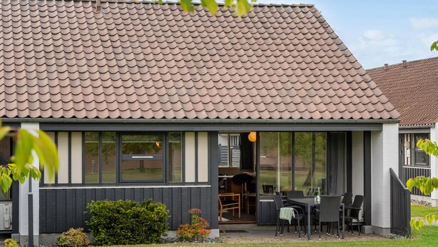 Una casa moderna con techo de tejas, ventanas grandes y un patio con mobiliario exterior.