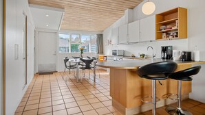 Una cocina moderna con una isla central, armarios blancos y techo de madera.