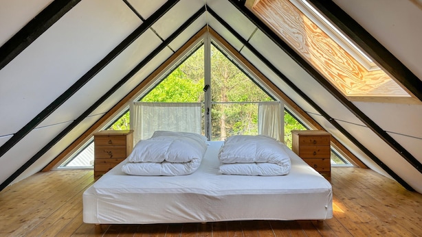 A bedroom with a bed, wooden nightstands, and large windows in a triangular attic space. - 2 bedroom cozy home in Fur (Fur)