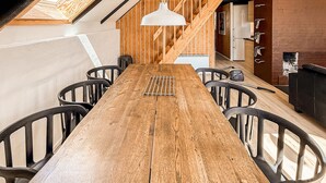 A long wooden dining table with chairs, a hanging light fixture, and a kitchen area with a refrigerator and cabinets. - 2 bedroom cozy home in Fur (Fur)