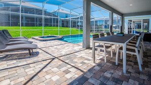 A covered patio area with a pool, outdoor seating, and a view of a house.