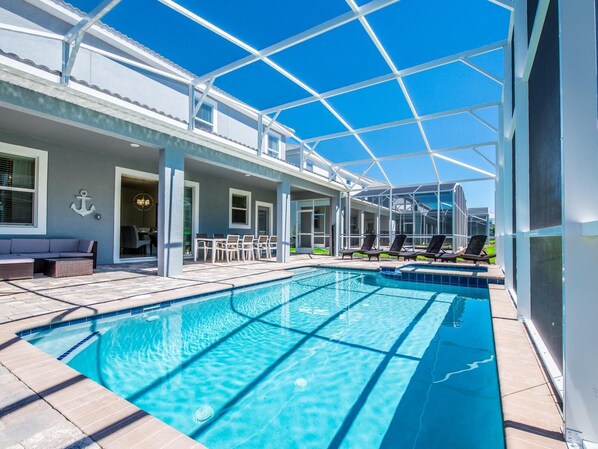 Una piscina con cerramiento de vidrio, mobiliario exterior y vistas del entorno.