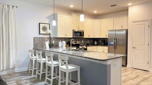 A modern kitchen with a central island, bar stools, stainless steel appliances, and a tiled backsplash.
