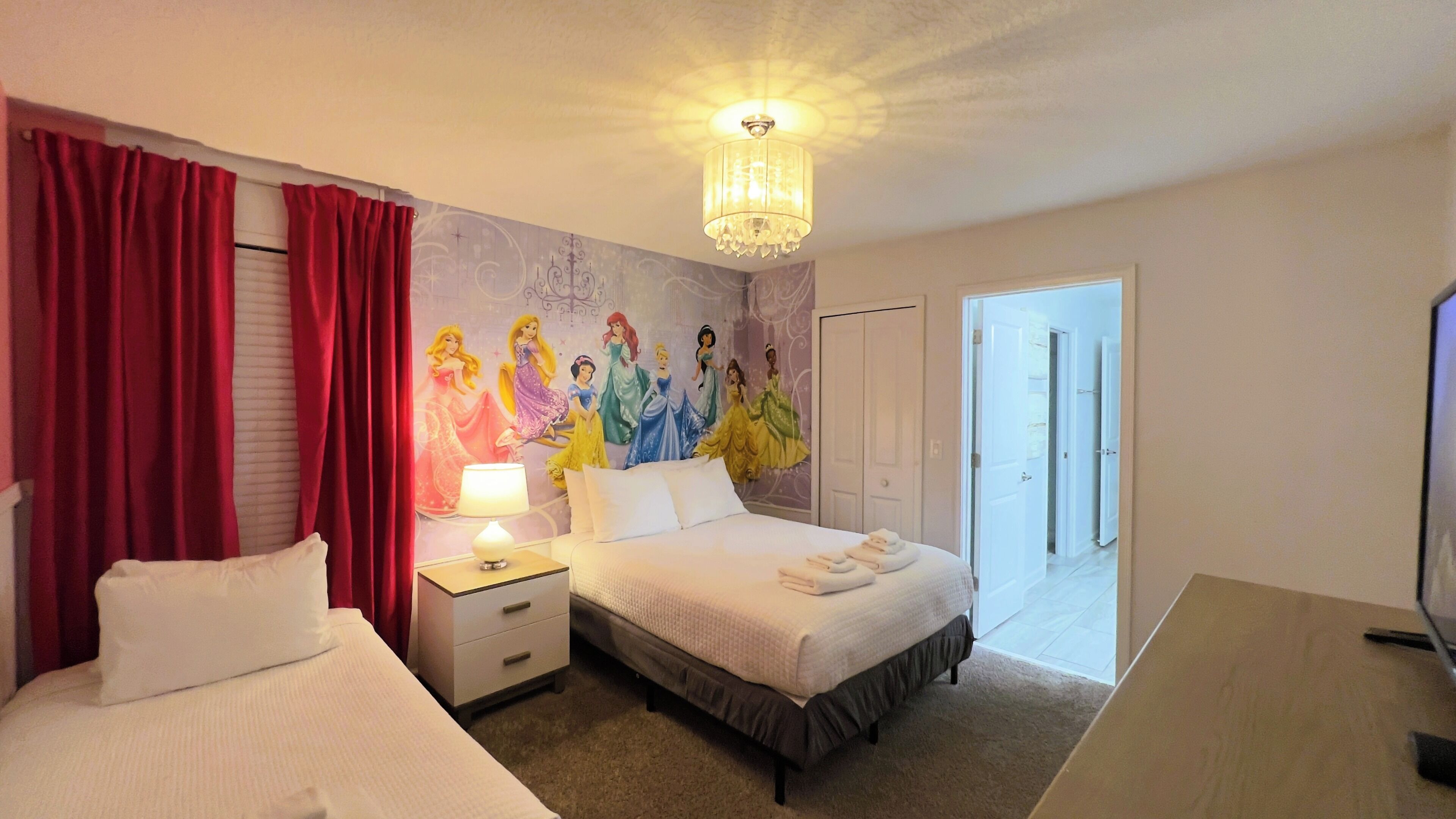 A hotel room with two beds, a mural of princesses on the wall, a chandelier, and a door leading to a balcony.
