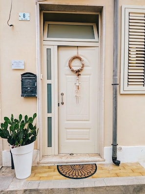 Une porte blanche ornée d’une guirlande, un pot de fleurs et une boîte aux lettres fixée au mur.