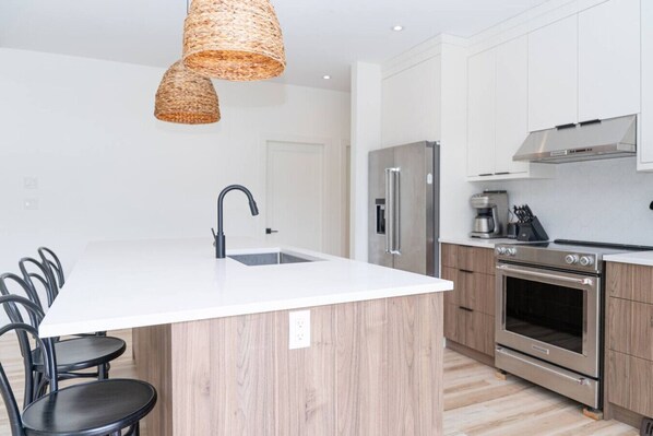 Una cocina moderna con una isla central, electrodomésticos de acero inoxidable y un comedor con sillas negras.
