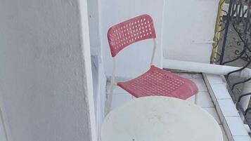 A small balcony with a white table and two red chairs.