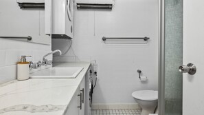 A modern bathroom with a white sink, mirror, and toilet. There are towel bars, a soap dispenser, and a shower area visible. - Welcome to "Home in the Snowies, your three-bedroom retreat nestled in the heart of Jindabyne, NSW (Jindabyne)