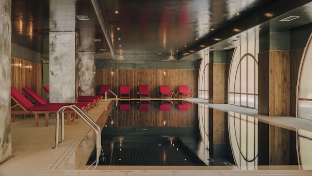 Una piscina interior moderna con una pared de madera y sillones reclinables rojos.