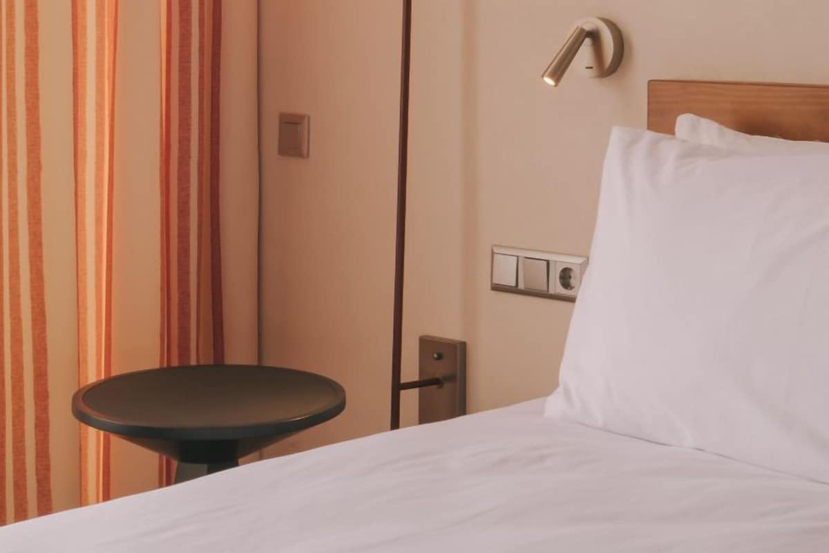 Una habitación de hotel con una cama, una mesita de noche, una lámpara y una cortina.
