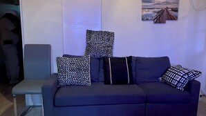 A dark-colored sofa with multiple pillows, a grey chair, and a painting on the wall. - MoBay Life (Montego Bay)