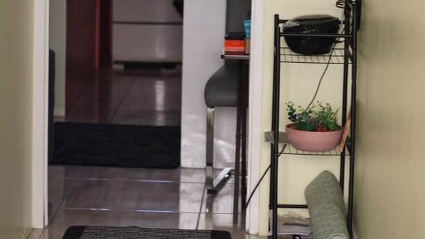 A hallway with a kitchen in the background, a black chair, a black shelf with a plant, and motivational wall art. - MoBay Life (Montego Bay)