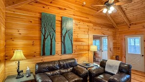 L’intérieur d’un chalet confortable, avec des murs en rondins, un canapé en cuir, une table basse en bois et deux tableaux accrochés au mur.