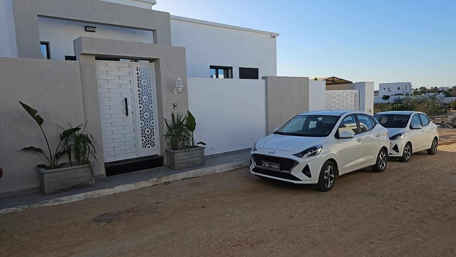 Una casa moderna con dos coches blancos estacionados al frente.
