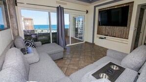 A modern living room with grey sofas, a flat-screen TV, and a sliding glass door leading to a balcony with a view of the ocean. - Bonita 602 (Puerto Peñasco)