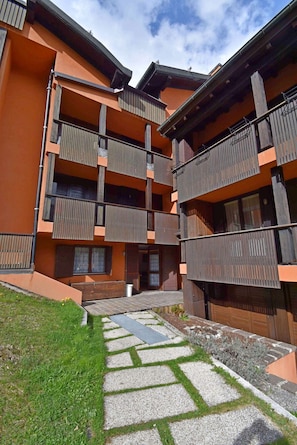 Un immeuble à plusieurs étages doté de balcons, d’un chemin pavé de pierres et d’une zone herbeuse.