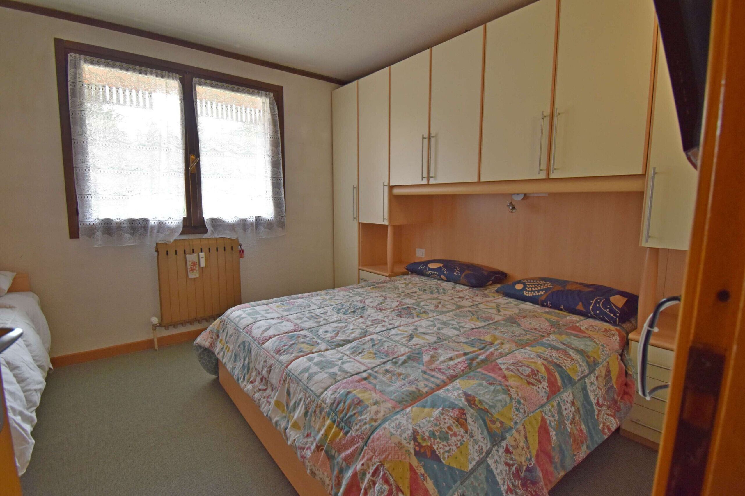 Une chambre à coucher avec un lit, une fenêtre avec des rideaux et des armoires encastrées en bois.