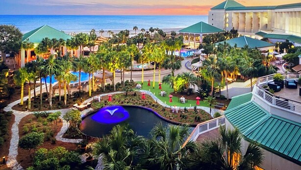 A resort with a pool, palm trees, and a view of the ocean.