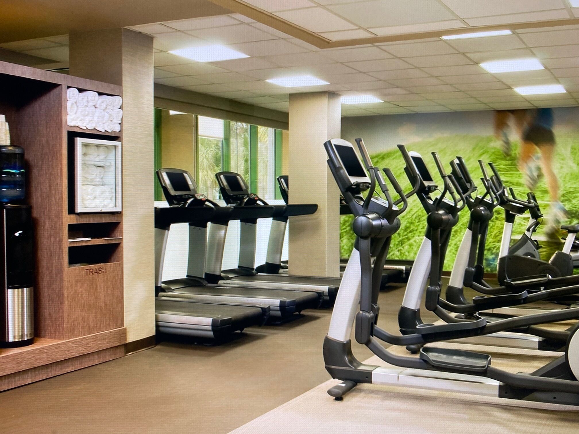 Un gimnasio con cintas de correr, un basurero y un dispensador de agua.