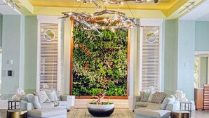 A modern lobby with two sofas, a large wall-mounted plant, and a unique chandelier.