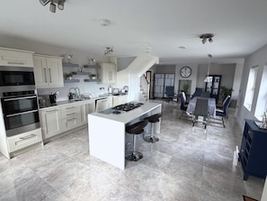 A modern kitchen with a central island, built-in ovens, and a dining area with a large clock.