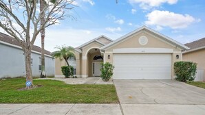 A single-story house with a garage, a front yard with a tree and shrubs, and a clear sky.