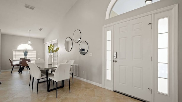 A spacious dining area with a high ceiling, a large window, and a door with a security system.