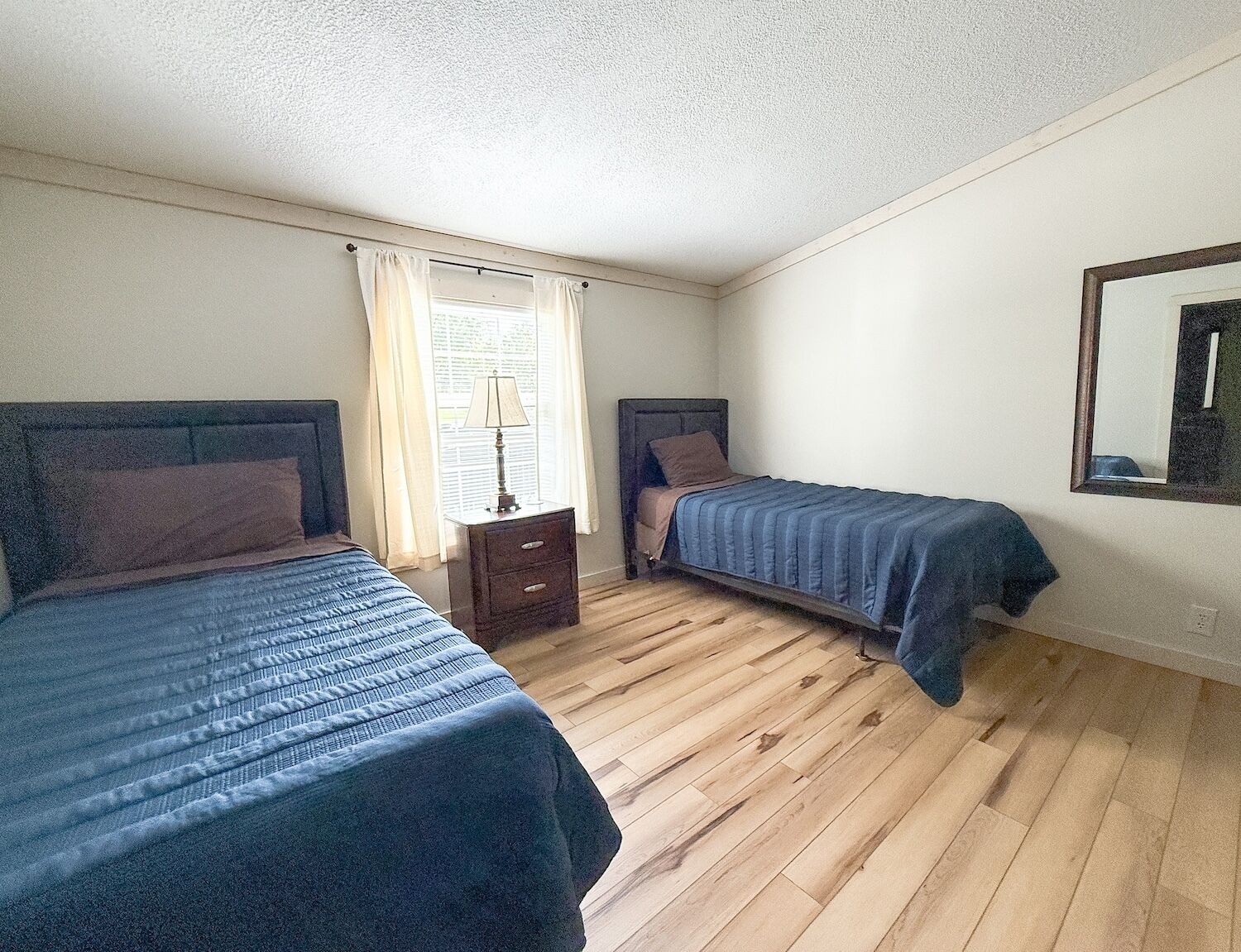 A room with two beds, a nightstand, a lamp, and a window with curtains.