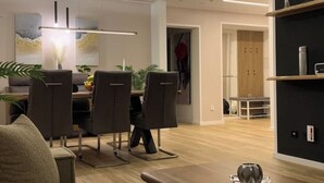 Een moderne eethoek met een tafel, stoelen, een hanglamp en een boekenplank met decoratieve objecten.