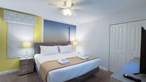 Une chambre d’hôtel comprenant un lit, des lampes de chevet, un ventilateur de plafond, une fenêtre avec des stores, un mur orné d’un motif décoratif et une porte.