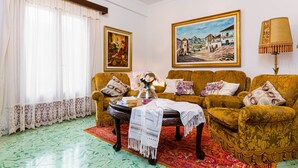 A living room with two sofas, a coffee table, and a chandelier. There are paintings on the walls and a window with curtains. - YourHouse Ca Na Fonoy (Santa Margalida)