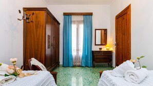 A hotel room with two beds, a wooden wardrobe, a dresser, a mirror, and a window with blue curtains. - YourHouse Ca Na Fonoy (Santa Margalida)