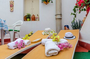 Un transat avec des serviettes et des fleurs, une chaise blanche et des objets décoratifs accrochés au mur.