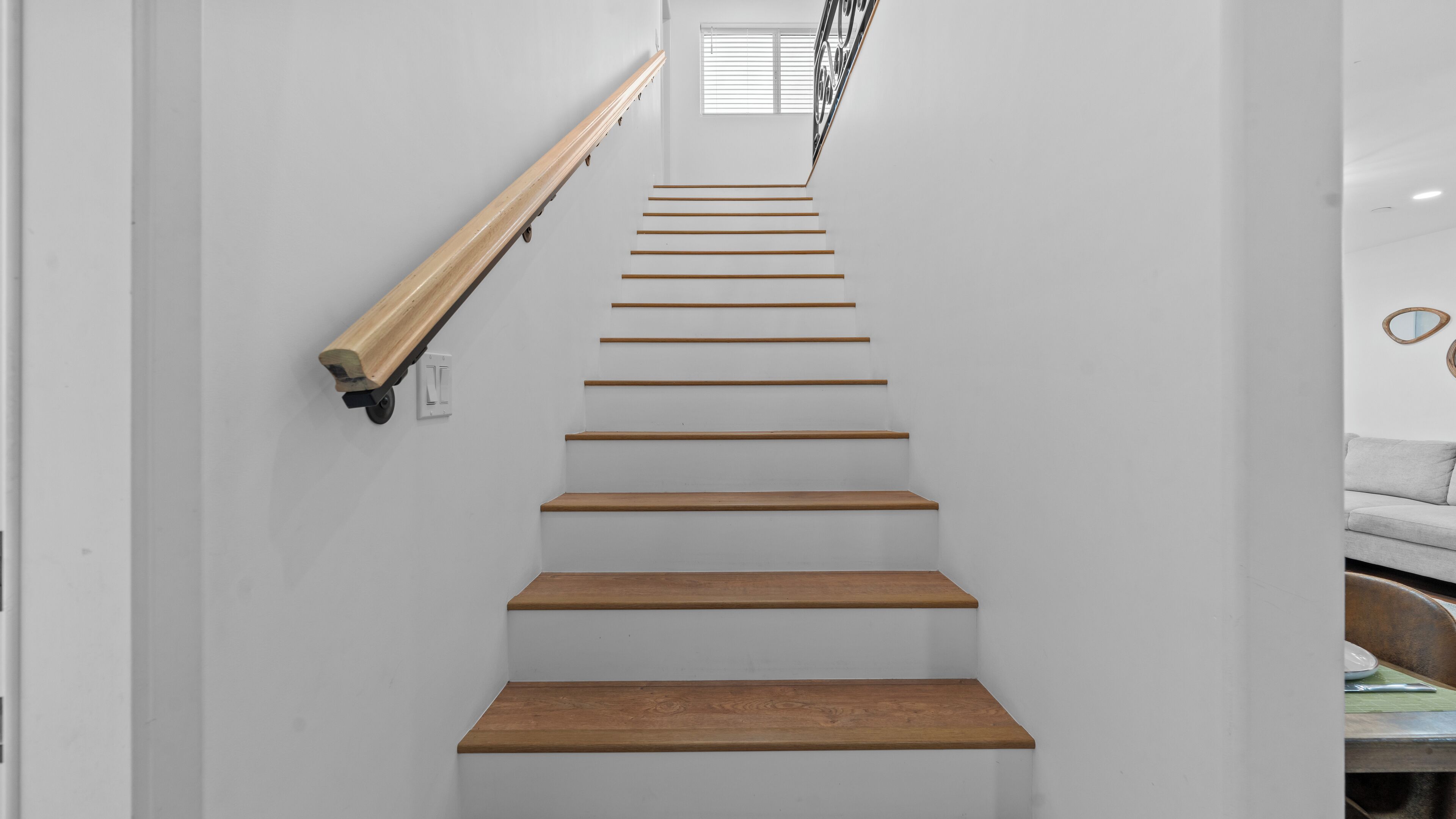 A staircase with wooden steps and a handrail, leading to a room with a window and a sofa.