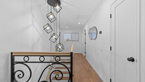A staircase with a wooden handrail and black metal balusters, leading to a room with white walls, a wooden floor, and a window with blinds. - One World House with King Bed (Colton)
