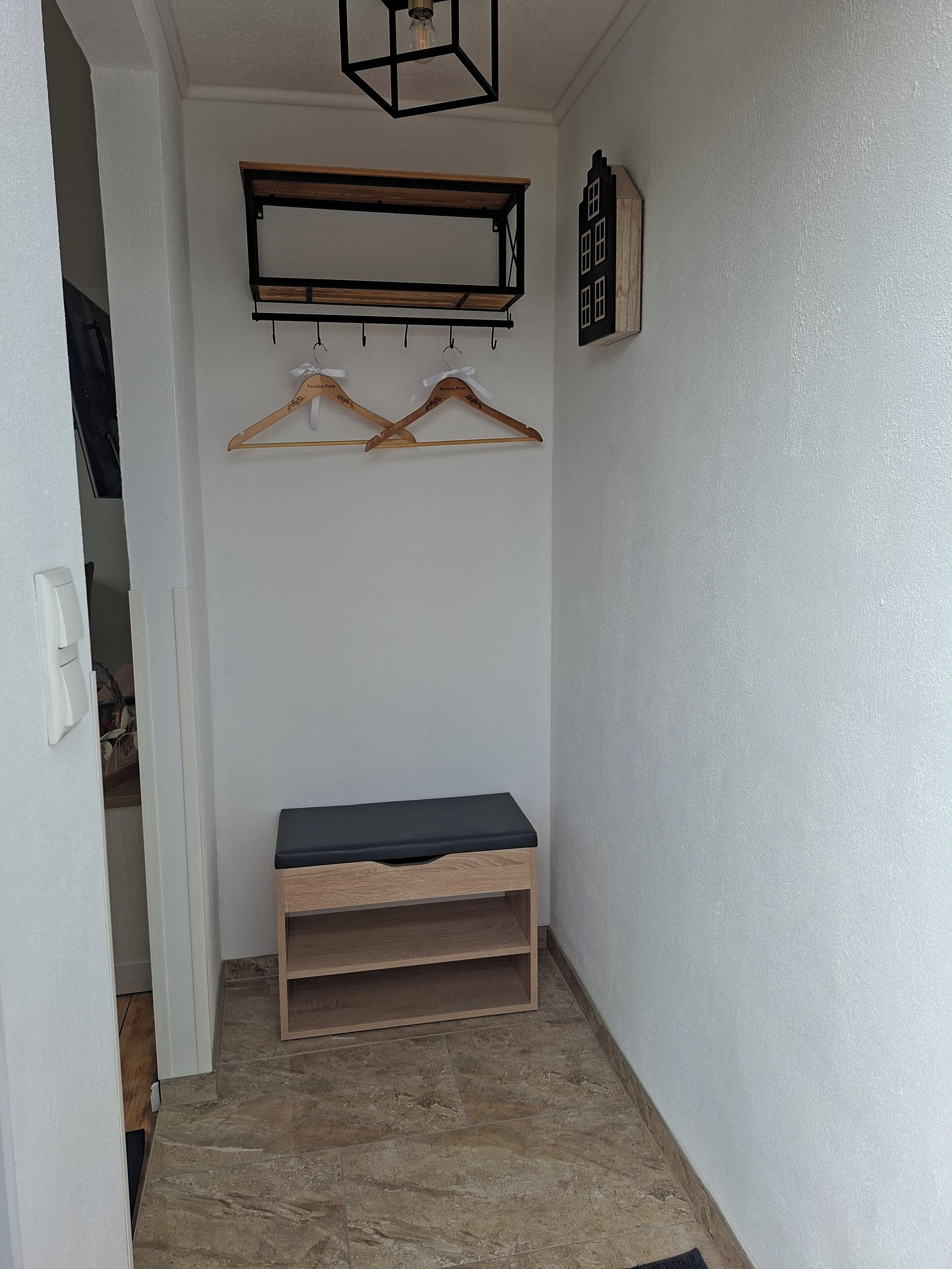 Un pasillo con un banco, perchas de madera y un estante en la pared.