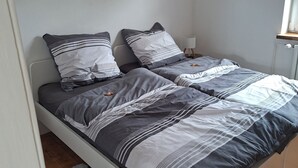 Ein Schlafzimmer mit Bett, Kissen, einem Nachttischchen, einer Lampe und einem Wandbild.