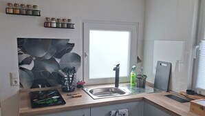Eine moderne Küche mit Spüle, Arbeitsplatte und Schränken. Gewürze befinden sich auf einem Regal über der Spüle und ein Handtuch hängt an der Schranktür.